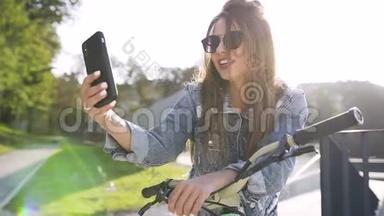 带着自行车戴太阳镜的漂亮开朗的高加索女孩的肖像，在<strong>手机</strong>上拍自拍照片。 户外<strong>活动</strong>